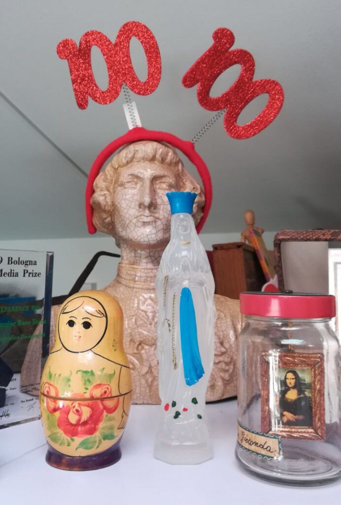 L'immagine di un acquasantiera di Lourdes vicino a una matrioska di legno e a un vaso di vetro con dentro la Gioconda